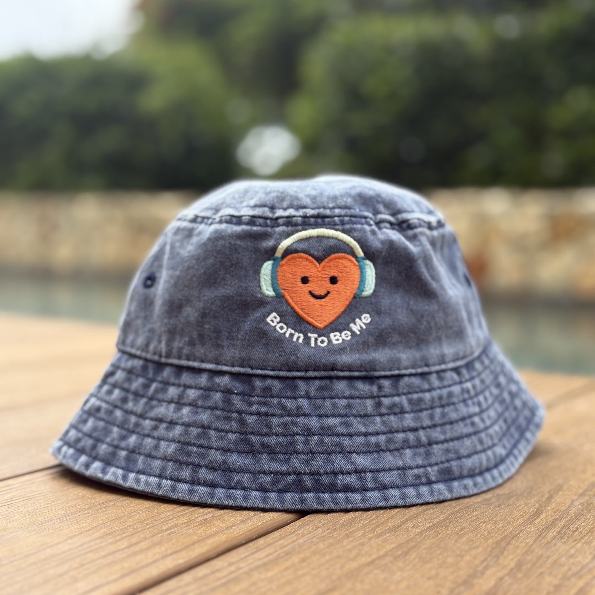 Blue bucket hat with a heart and text design on a wooden surface with a blurred natural background